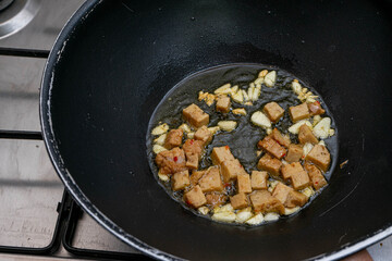 Golden-brown seitan cubes sizzling in a frying pan with garlic and olive oil. A healthy, plant-based protein meal idea, perfect for vegan or vegetarian cuisine concepts.