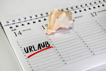 Tischkalender mit der Eintragung Urlaub in deutscher Sprache und einer Muschel als Symbol für...