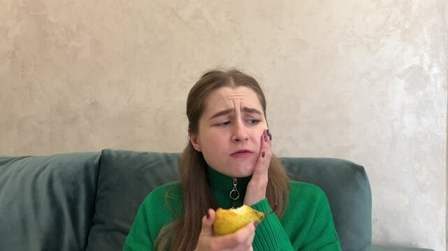 Woman is suffering from tooth pain after biting into a pear and is holding her face with a painful expression