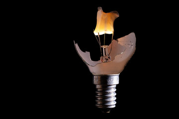 gebrochene Glühlampe mit durchbrennender  Glühwendel, Wolframdraht vor schwarzen Hintergrund und komplett sichtbaren Lampengewinde E29