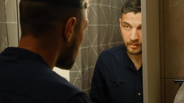 Morning bathroom refreshment routine concept. A young Caucasian man stands in front of the bathroom mirror and washes his face, then wipes his face with a towel