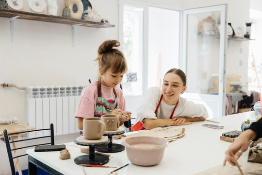 Girl enjoys pottery class with instructor in bright studio space