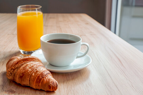 Generated image, un café un croissant et un verre de jus d'orange sur une table en bois, lumière naturelle venant de la fenêtre 