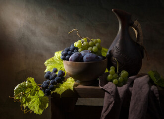 Still life with grapes and plums in a wooden bowl in the basement