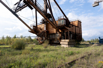 Fototapeta premium Abandoned Rusty Excavator Surrounded by Overgrown Grass and Trees