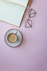 top view photo of cup of coffee, glasses and notebook on pastel background. 