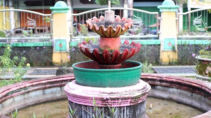 A multi-tiered fountain, adorned with vibrant colors, stands in a garden setting, its base surrounded by a circular pool.