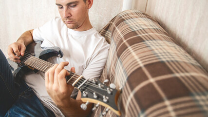 Musical hobby. Guitar skill. Man sitting on sofa playing string instrument enjoying learning chords...