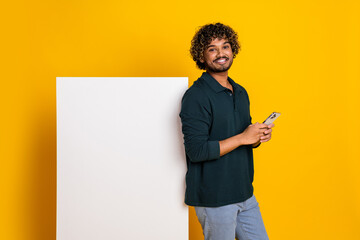 Cheerful young man in casual wear using smartphone against a vibrant yellow background, perfect for...