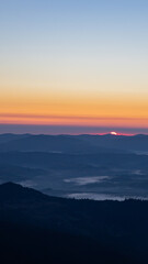 Dawn in the mountains, the sun barely peeking out from behind the horizon, white clouds spreading across the valleys