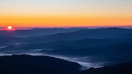 Obraz premium the red sun rises over the mountains, a thick fog still lies in the dark lowlands