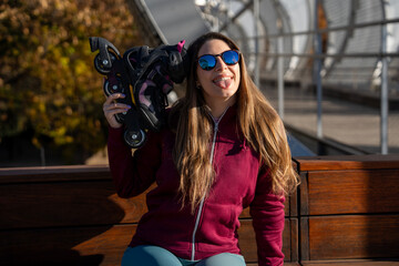 Young woman showing tongue while holding inline skates outdoors
