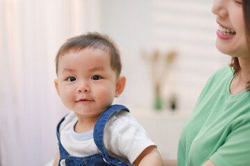 A smiling and happy mother holds her baby and plays in the house.