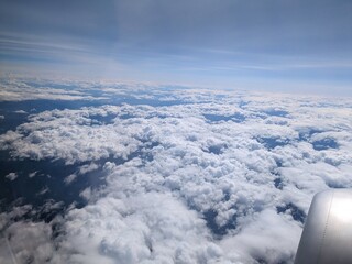 An airplane window. View of puffy cumulus clouds in the blue sky