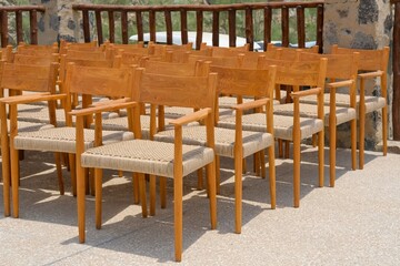 Group of empty wooden vintage chairs with rattan seats arranged in rows before an event. Many wooden outdoors armchairs. Public event furnishing
