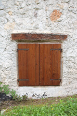 Finestra rustica chiusa con trave di sostegno e battenti di legno con muro di pietra e cemento