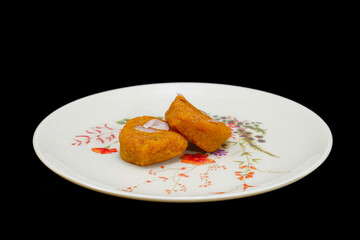 Two pieces of Mohanthal, a traditional Gujarati sweet dish, placed in a white dish with floral pattern, Isolate with Black Background