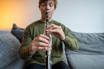 Clarinet player closeup. Clarinetist hands playing flute woodwind music instrument, sitting on couch at home, soft focus. Musical wind instruments. Guy plays the oboe in living room. Hobby. 