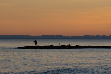 summer landscape sunset orange sky on Mediterranean coast silhouette fisherman fishing in...