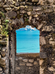 Window in stone wall of ancient Bastione di Riva framing panoramic view of idyllic lake Garda, Trentino, Italy. Landmark in lakeside town Riva Del Garda in summer. Tourist travel destination