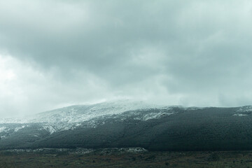 A scenic mountain in Spain, crowned with a dusting of snow. Cloudy sky add dramatic atmosphere.