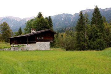 Baita di legno e pietra con prato bosco montagne e cielo
