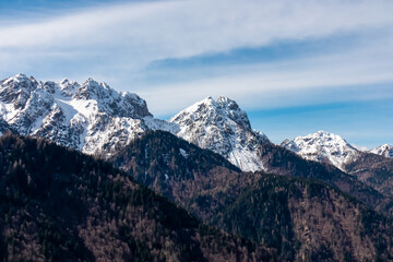 Panoramic view of snow capped mountain peaks of Julian Alps seen from Monte Nebria Cima Est, Friuli Venezia Giulia, Italy. Wanderlust in alpine wilderness in early spring. Hills covered with forest