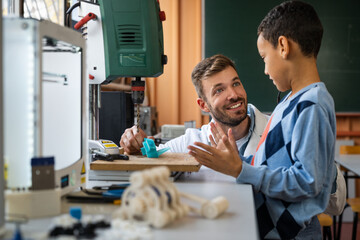 A male teacher guides a diverse young student through a 3D printing project in a well-equipped STEM classroom.