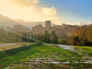 Besalú, Girona. Pueblo antiguo bajo la lluvia al atardecer, con una iglesia prominente y montañas...
