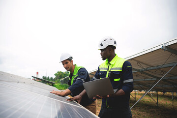 Two men are working on a solar panel, one of them holding a laptop. Concept of teamwork and...