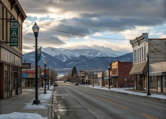 Fototapeta premium Deserted small town main street with distant snow-capped mountains, partly cloudy sky, past liveliness signs, and winter colors.