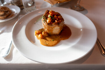 A puff pastry filled with seafood, topped with a creamy sauce and garnished with herbs, served on a white plate with a rich brown gravy.