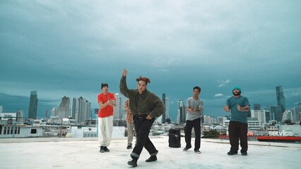 Hispanic hipster dancing surrounded by multicultural friend at city view with blue sky. Group of street dancer performing at rooftop. Active, fun, happy atmosphere. Outdoor sport 2024. Hiphop.