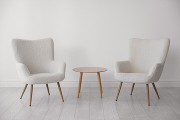 Fototapeta premium Soft armchairs and coffee table near white wall indoors