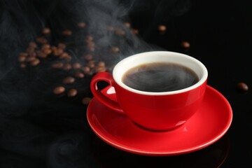 Red cup with coffee and roasted beans on black background, closeup