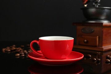 Red cup with coffee, vintage grinder and roasted beans on black background