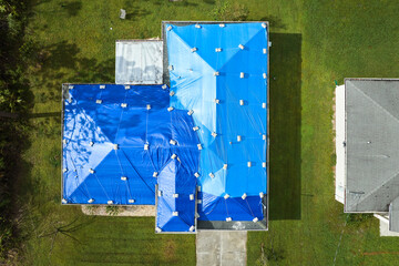 Top view of leaking house roof covered with protective tarp sheets against rain water leaks until...