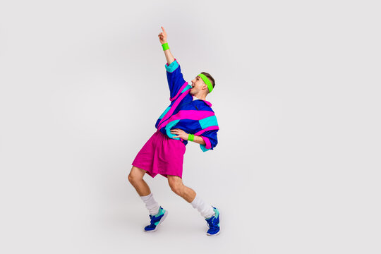 Energetic young man in colorful retro activewear pointing upwards while expressing joy against a grey background