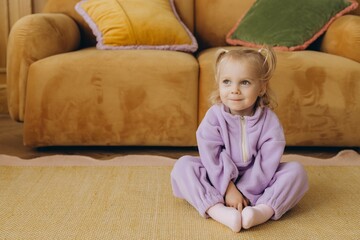 Smiling toddler wearing purple jumpsuit sitting on carpet in living room