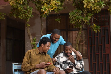 three students standing together in a school courtyard. They are engaged with their smart phones, absorbed in their devices.