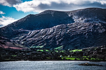 A majestic mountain rises dramatically above a tranquil body of water, with lush green fields...