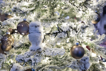 A festive Christmas tree adorned with glowing lights, ornaments, and white owl decorations, surrounded by wrapped gifts in a cozy indoor setting.