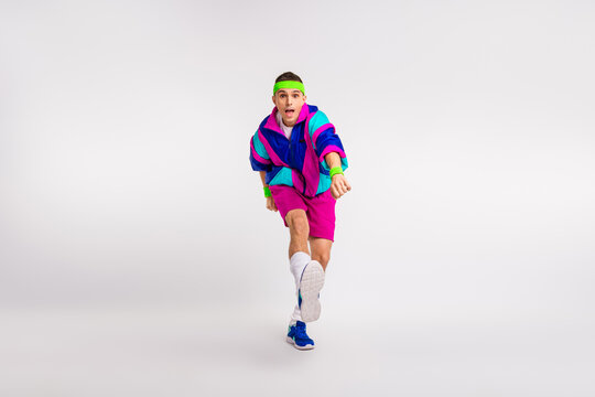 Energetic young man in vibrant retro activewear kicking with enthusiasm against a minimalist background