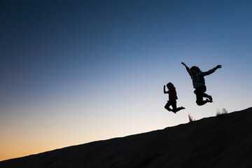 Black silhouette at sunset sky background. Happy family - kids running and jumping high in the air from sea beach sand dune. Active people, outdoor activity on tropical summer vacations with children