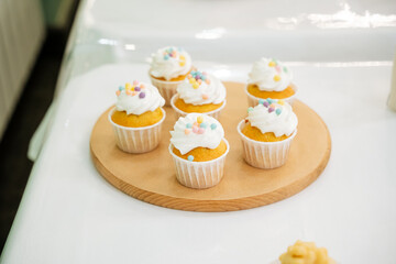 A rustic wooden cutting board showcases an array of delightful cupcakes, each with creamy white frosting and colorful sprinkles, forming an impressive dessert centerpiece