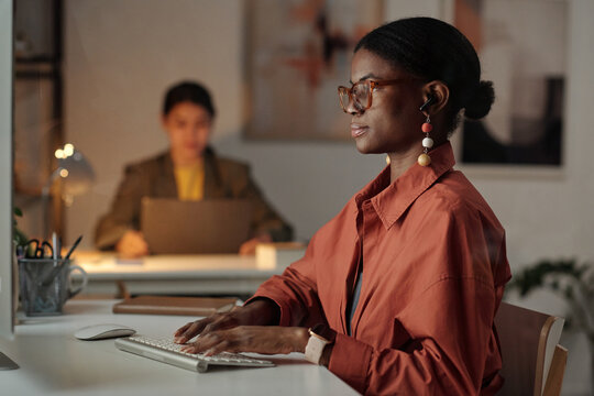 Side view of young African American female white collar worker looking at laptop screen and typing on keypad