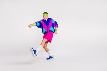 Fototapeta premium Young man in colorful retro activewear energetically performing a dynamic exercise on a white background