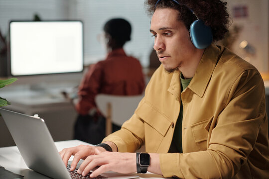 Elegant serious man with headphones watching online video and using neuronet for creating new digital content