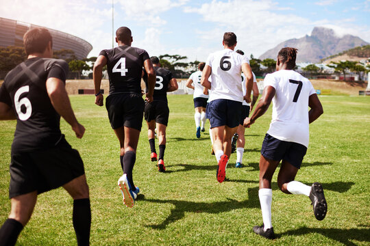 Back, people and running on field for rugby, tournament and start of competitive game on grass. Sport, fitness men or team at stadium for competition, match or community challenge in outreach program