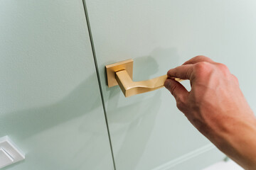 A person is elegantly opening a door that boasts a beautifully designed gold handle, which is often...